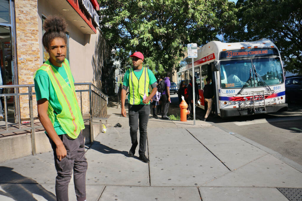 2022 09 23-e lee-robert lynch paul t jackson-philadelphia susquehanna and broad-front line dads Two people wearing safety vests stand at a street corner. A SEPTA bus and passersby are visible in the background.
