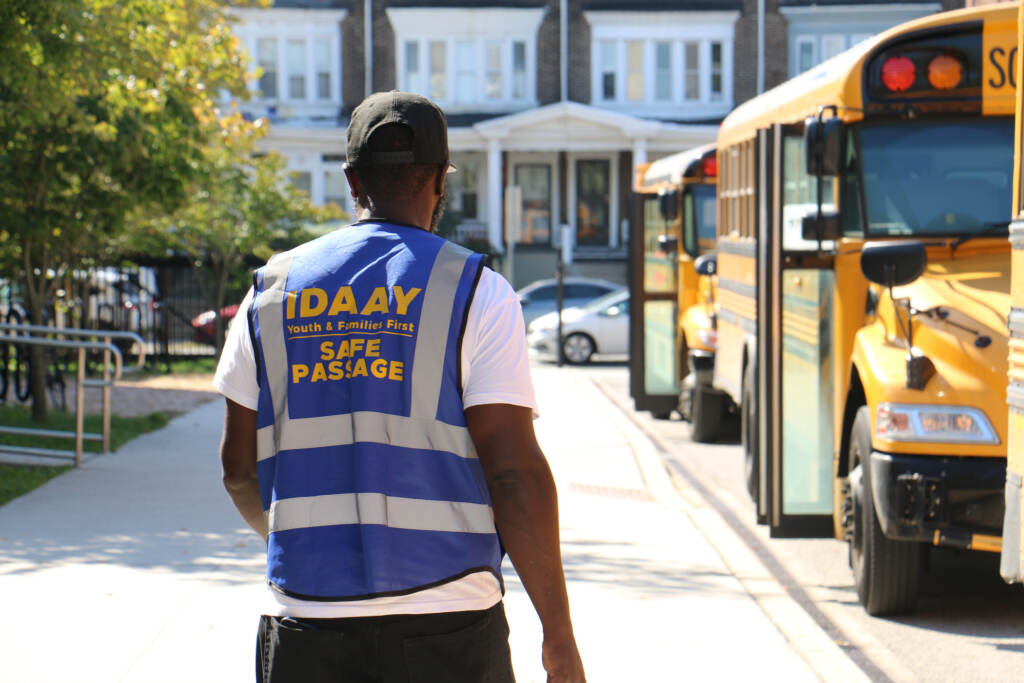 2022 10 07-e lee-malik smith-west philadelphia high school-safe passage school buses A person wearing a security vest walks near school buses.