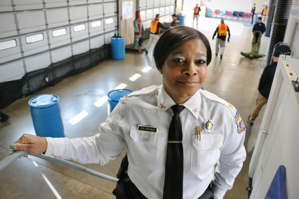 2023 02 06-e lee-altovise love craighead-philadelphia police training center-trauma informed policing desk training Altovise Love-Craighead smiles, paused on a staircase. Below her is a large space where police recruits are training.