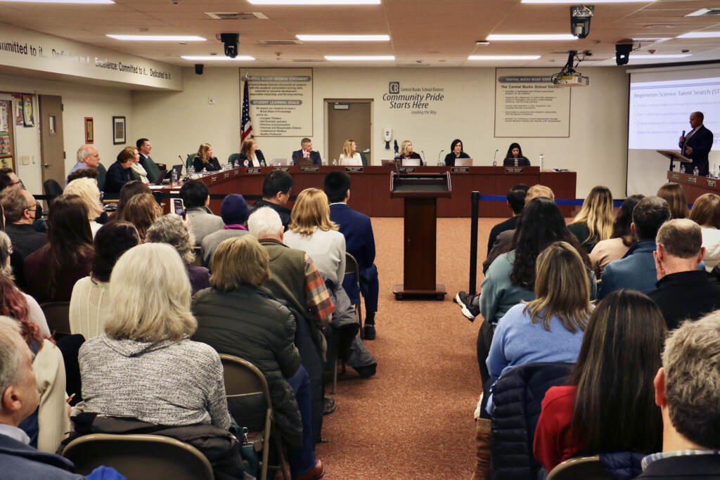 2023 02 07-e lee-doylestown pa-central bucks school board crowd A group of people sit in chairs, and other people sit in a table at the front of the room.