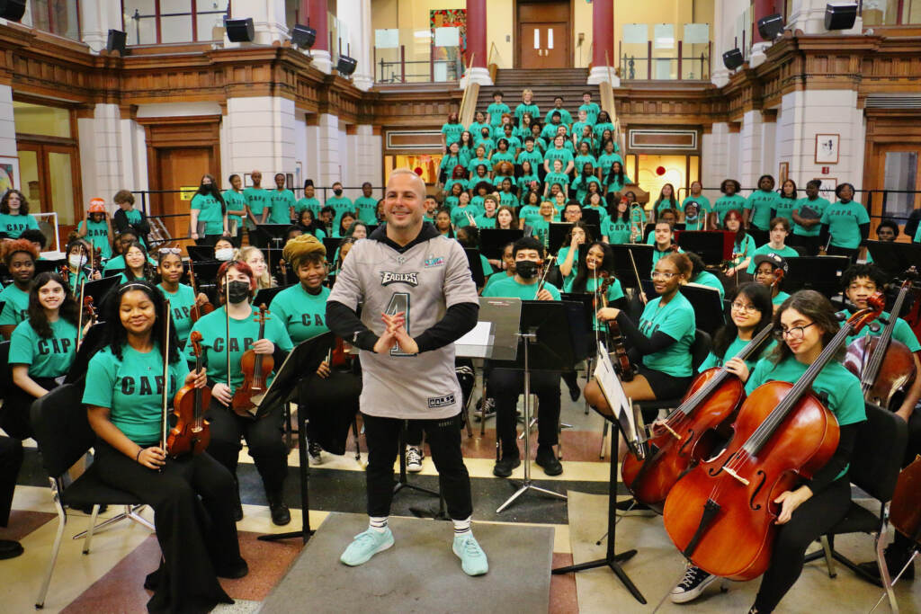 2023 02 10-e lee-yannick nezet seguin-philadelphia capa high school-fly eagles fly poses The conductor poses with a group of students in an orchestra.