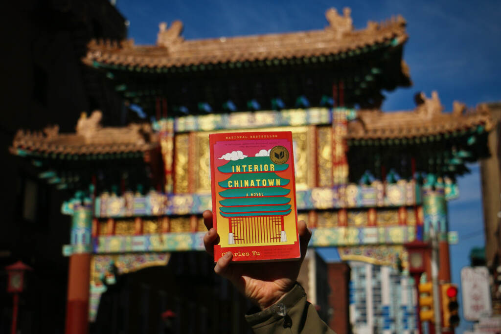 2023 02 14-e lee-philadelphia- one book interior chinatown charles yu A book is held up in front of the ornate gateway in Philadelphia's Chinatown.