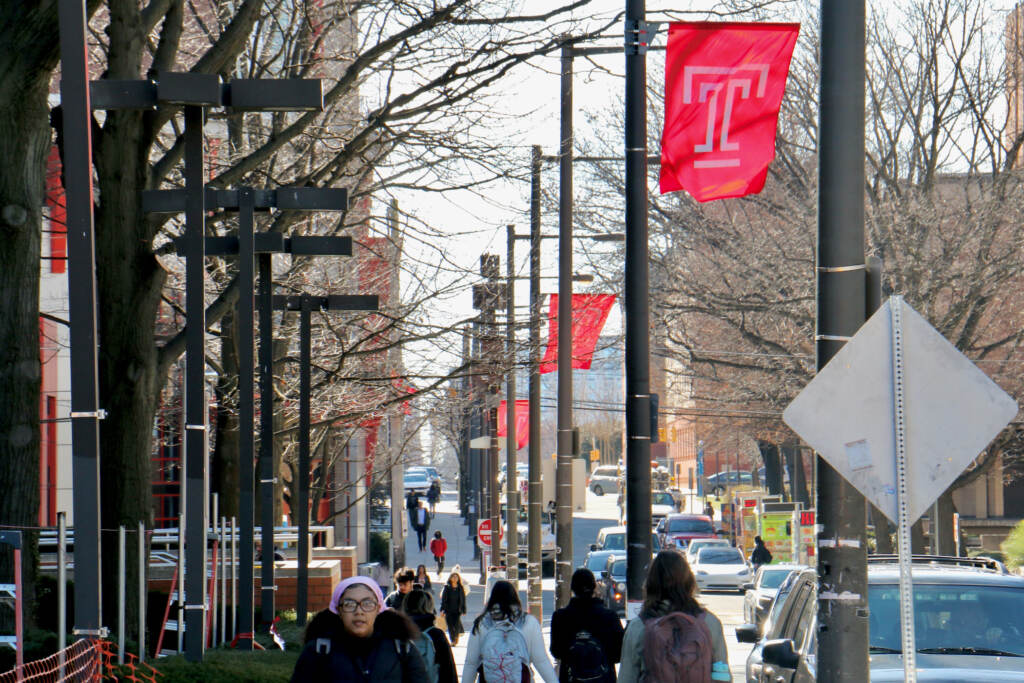 North 13th Street on Temple University campus. (Emma Lee/WHYY) People walk by signs emblazoned with Temple's logo.
