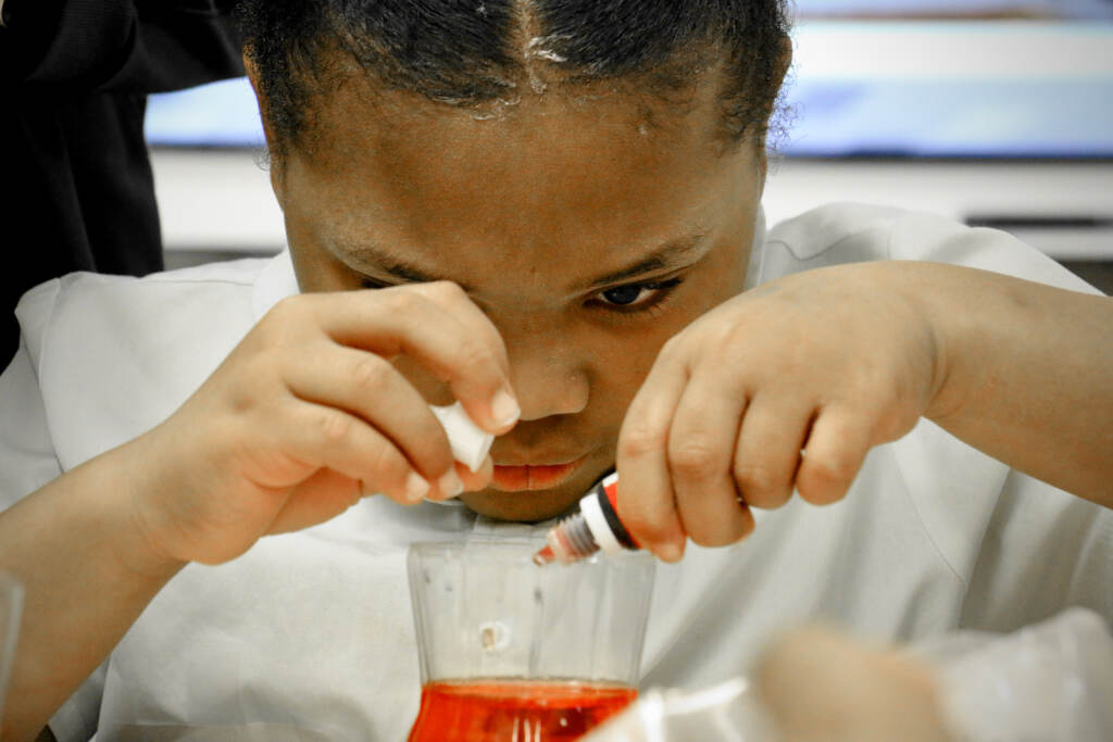 A close-up of a little girl adding red dye into a test tube.