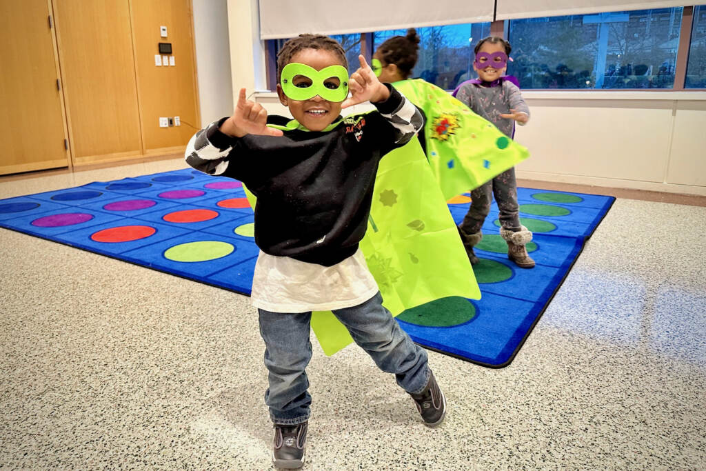 A young boy poses with a superhero cape and mask.