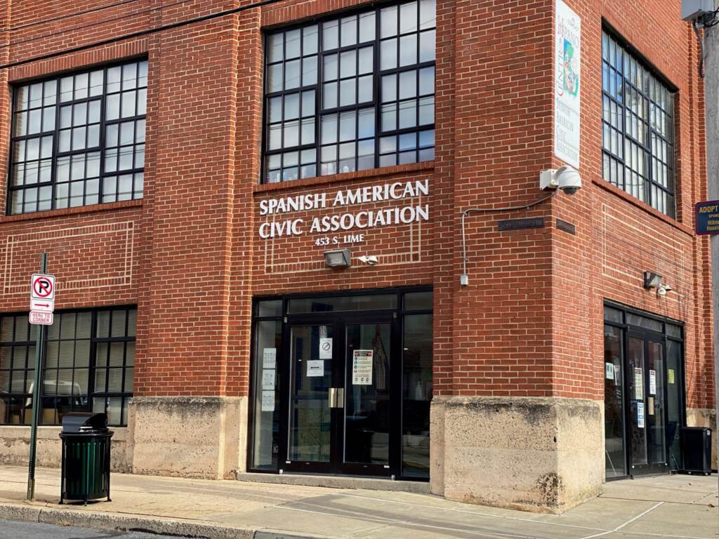 SACA-1440×1080 A view from the sidewalk of a red-brick building with a sign that reads Spanish American Civic Association.