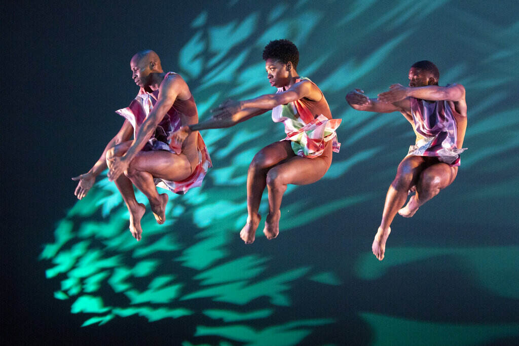 Alvin Ailey Dance Dancers leap in the air against a colorful backdrop.