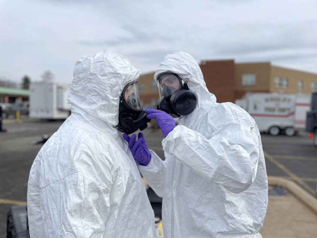 In this photo provided by the Ohio National Guard, ONG 52nd Civil Support Team members prepare to enter an incident area to assess remaining hazards in East Palestine, Ohio, on Feb. 7. Two people in hazmats suits check each others' masks.