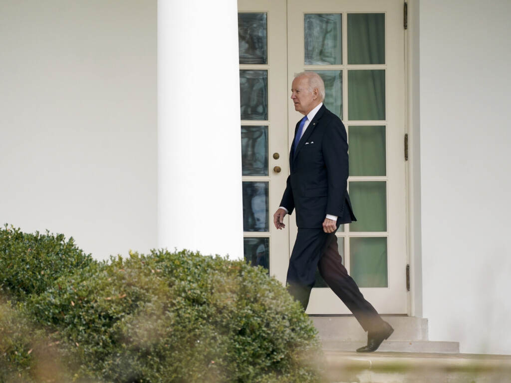Biden Biden walks in an outdoor corridor at the White House.