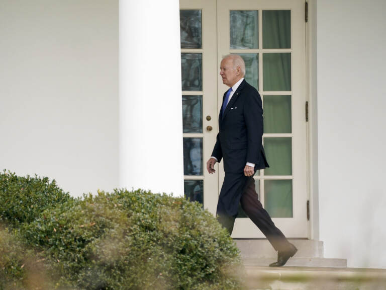 Biden walks in an outdoor corridor at the White House.