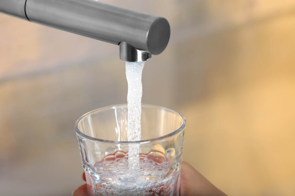 Woman Filling Glass With Tap Water From Faucet On Blurred Backgr Woman filling glass with tap water from faucet on blurred background, closeup