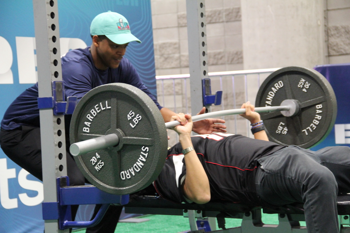 A person lifts a weight as a spotter looks on.