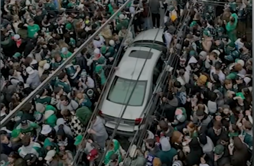 fundraiser-man-fix-car-north-philly An aerial view of a silver car surrounded by a large crowd of people wearing green.