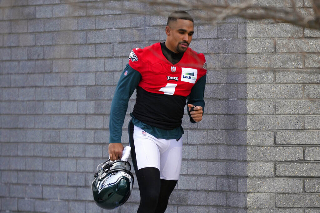 Super Bowl Eagles Football Jalen Hurts, wearing a red practice jersey, walks by a brick wall.
