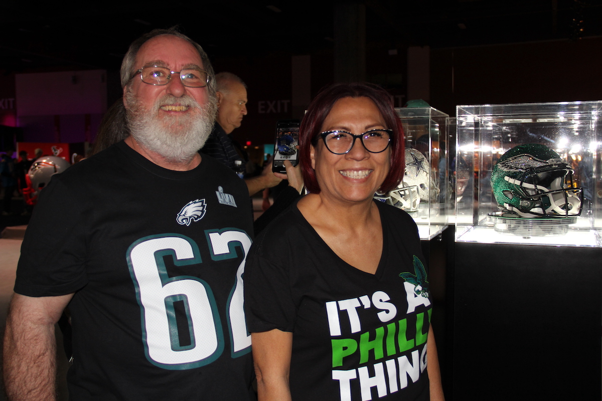 Two Eagles fans pose with a bejeweled Eagles helmet which is visible behind a glass display case.