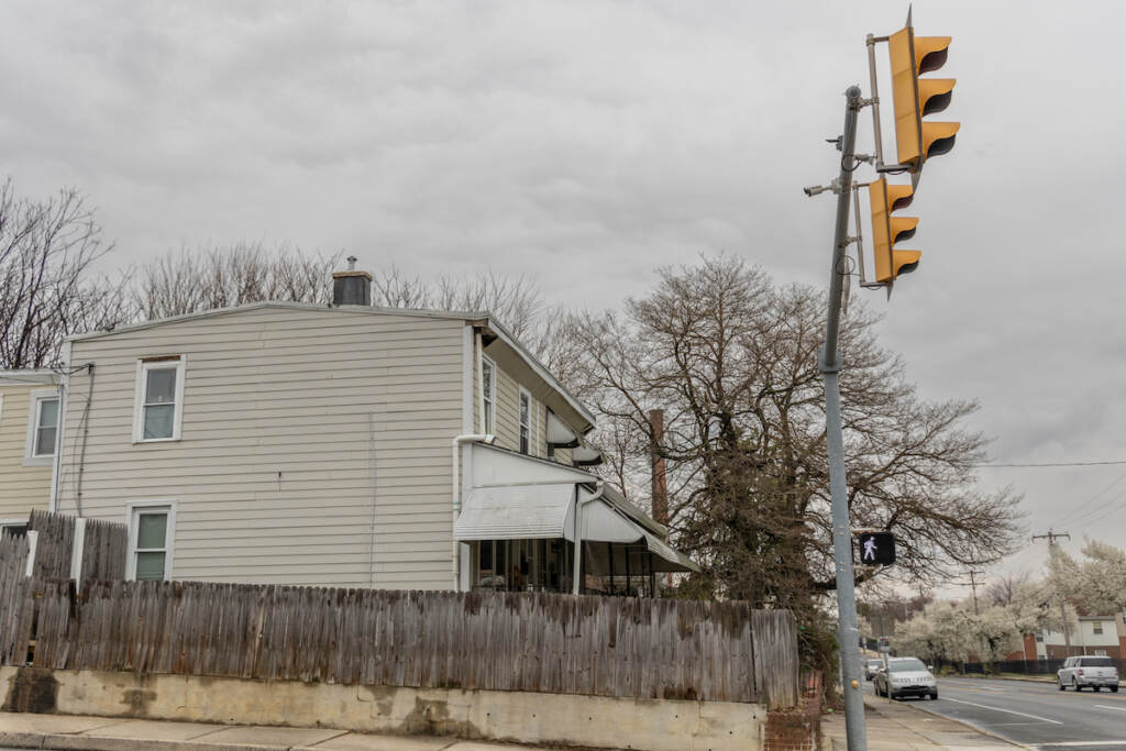 A security camera at an intersection is visible. A house and cars are visible in the background.