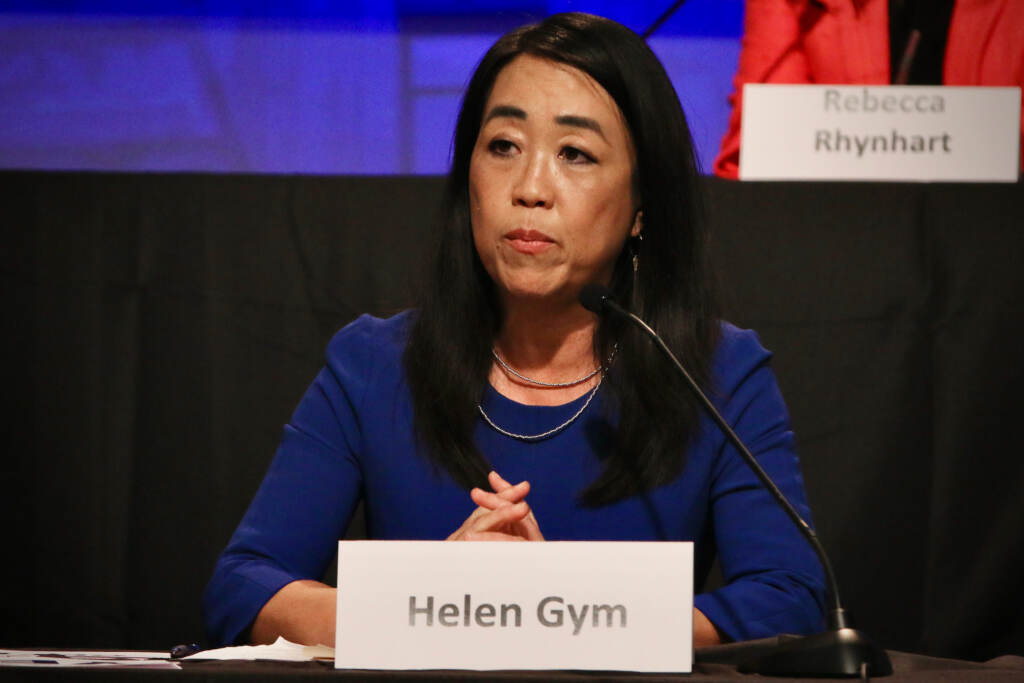 Helen Gym sits in front of a microphone and a sign with her name on it.