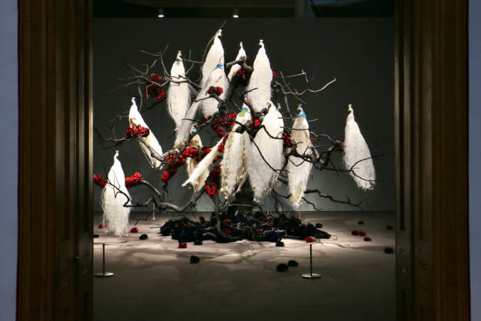 A tree full of taxidermied peacocks is on display.