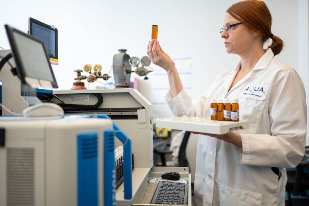 A scientist holds up a water sample at a testing station in a lab.
