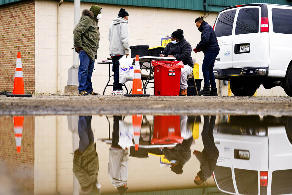 Opioid Crisis Settlement A group of people are seen from a distance standing around a folding table, outdoors.