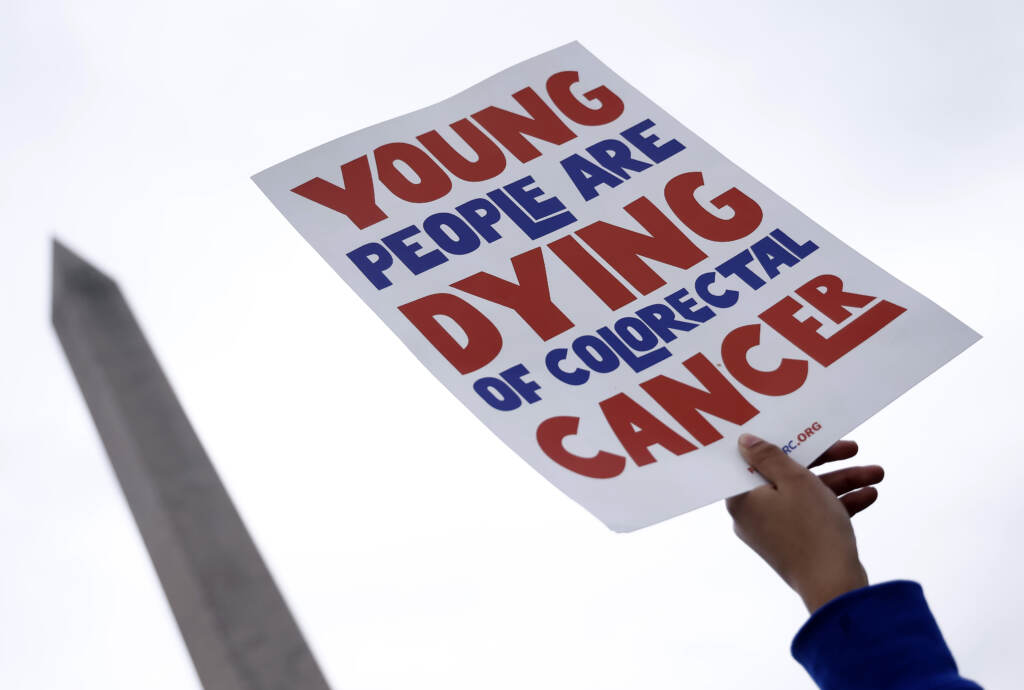 a person holding a sign that says 'Young people are dying of colorectal cancer'