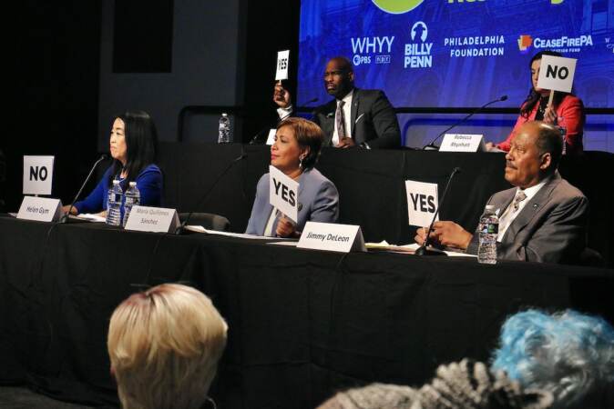 Mayoral candidates raise signs that read either yes or no as they sit at tables onstage during the forum.