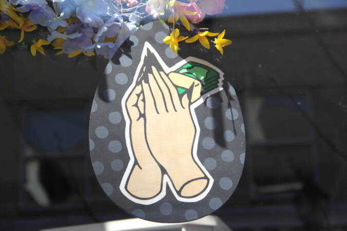 A two-dimensional egg design depicts hands clasped in prayer with dollar bills.