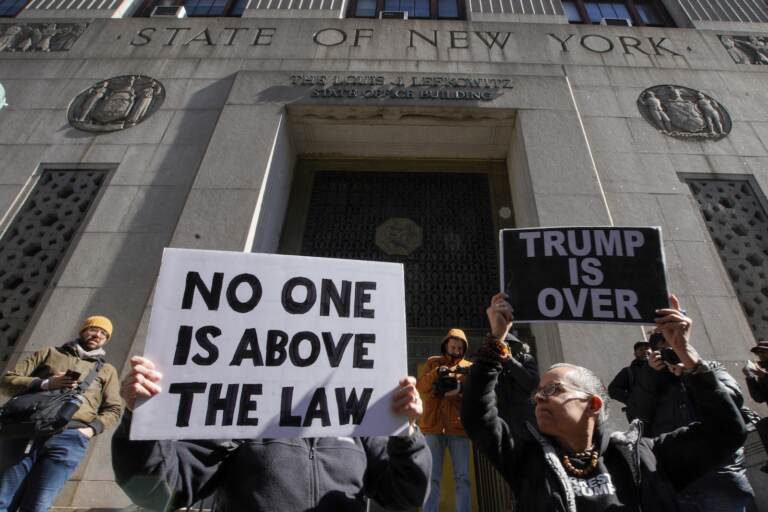 People hold up posters as part of a protest in front of the courthouse ahead of former President Donald Trump's anticipated indictment