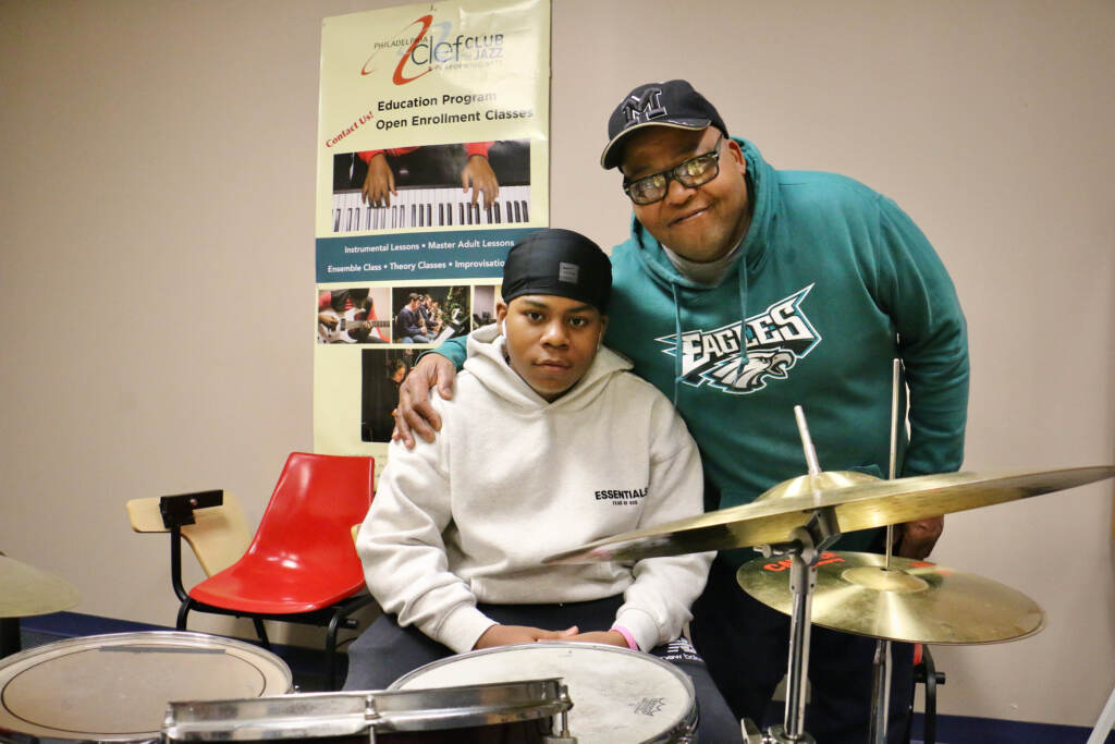 2023 04 01-e lee-elijah barnes michael barnes-philadelphia clef club- Michael Barnes embraces his 13-year-old son, Elijah, behind a drum set at the Clef Club.