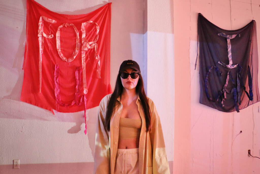 A person poses with tapestries hung on a wall.