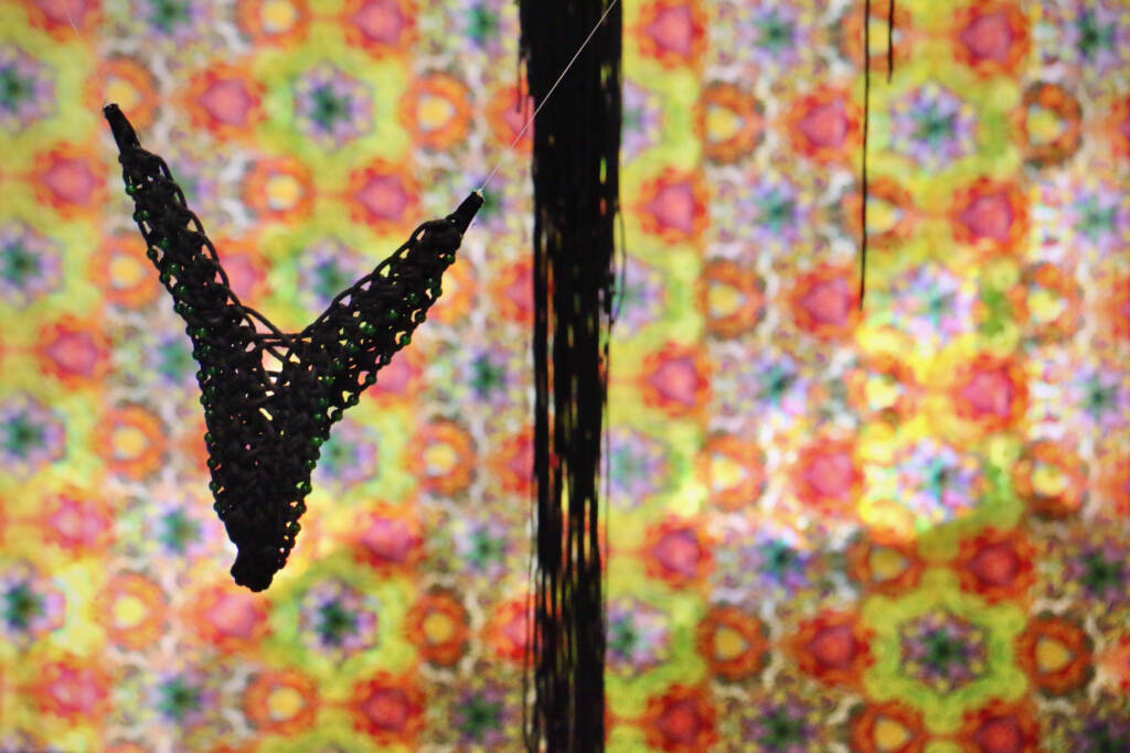 A piece of lingerie is hung in front of a brightly-colored yellow, pink, and orange curtain.