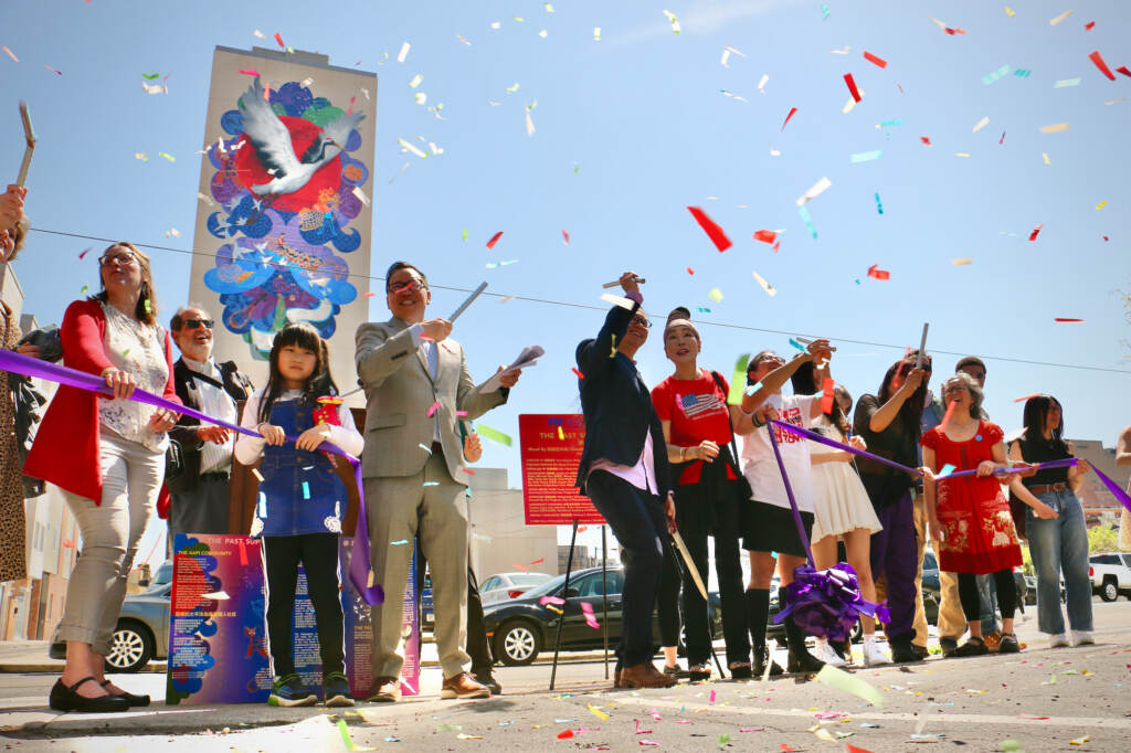2023 04 12-e lee-philadelphia crance chinatown community center-ribbon cutting Confetti is visible in the air as people celebrate in front of a mural on a building.