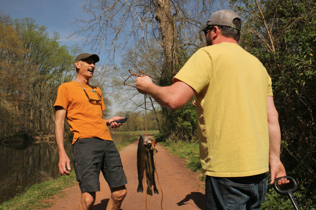 Neil King talking with a fisherman who is holding up fish he caught.
