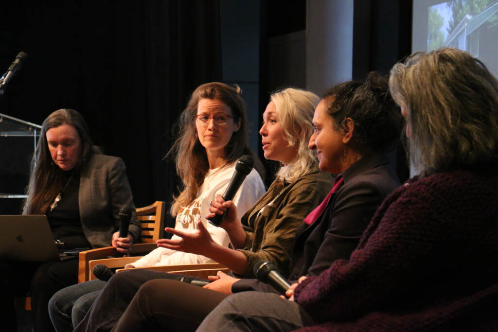 Sophia Schmidt speaks into a microphone as other panelists look on.