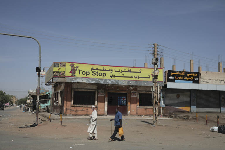 People walk past shuttered shops in Khartoum, Sudan