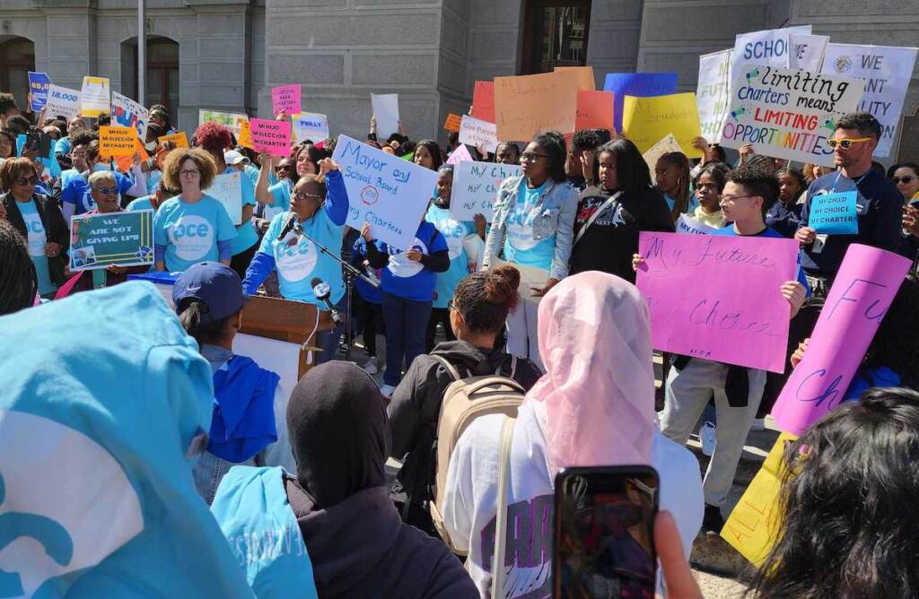 People gather around outside of City Hall, holding signs in support of charter schools.