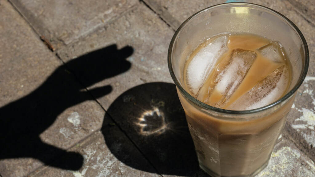 Shadow of a hand reaching for an iced coffee Shadow of a hand reaching for an iced coffee