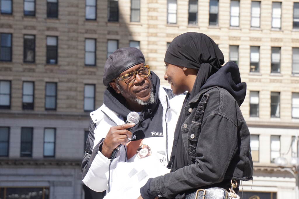 An older man holding a microphone for a teenager at a rally