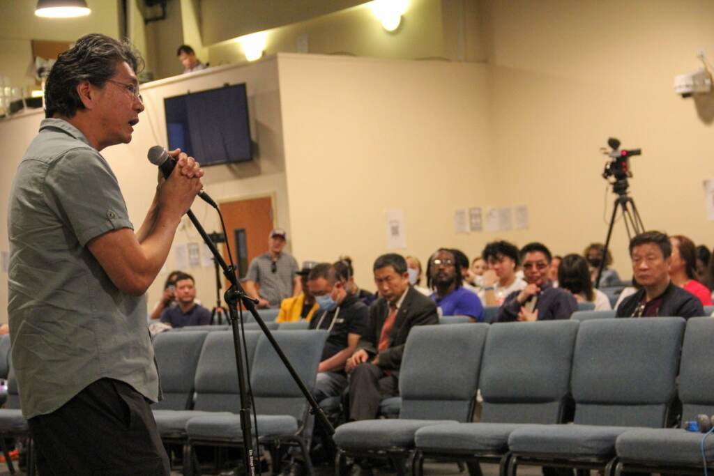 news-chinatownarena-aprilmtg-7-scaled QT Vietnamese Sandwich owner Michael Ha speaks into a microphone in front of a number of people seated in an audience.
