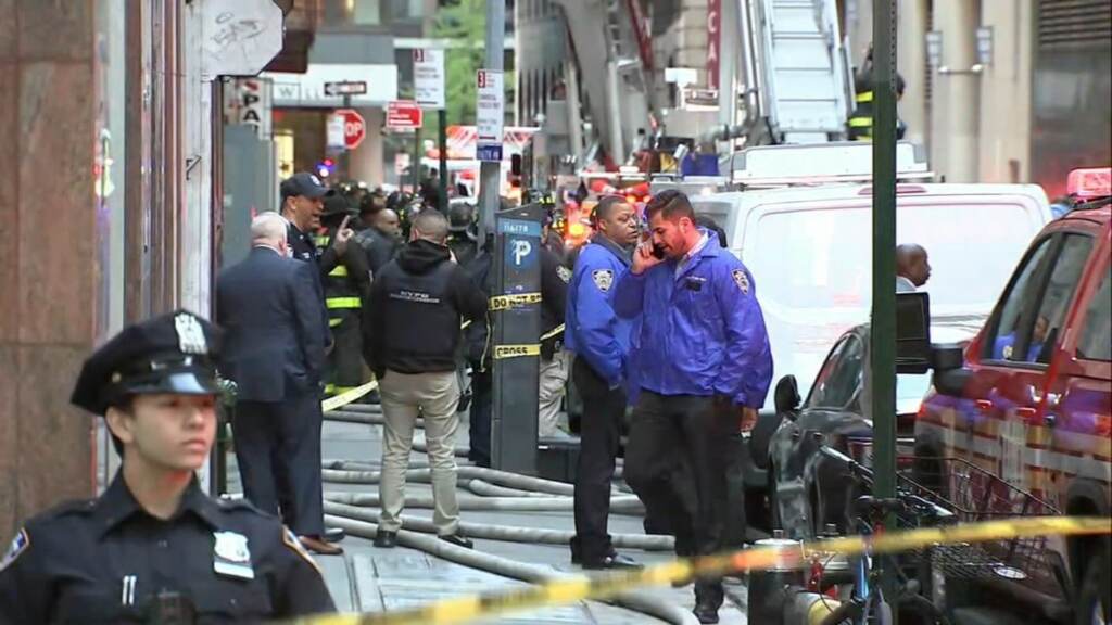 Bystanders and police officers stand near the site of a parking garage collapse.