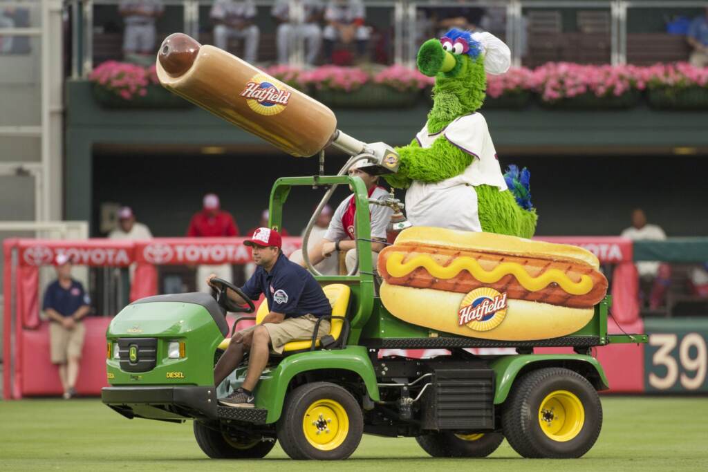 The Phillie Phanatic rides on a cart on field with the hot dog cannon in hand.