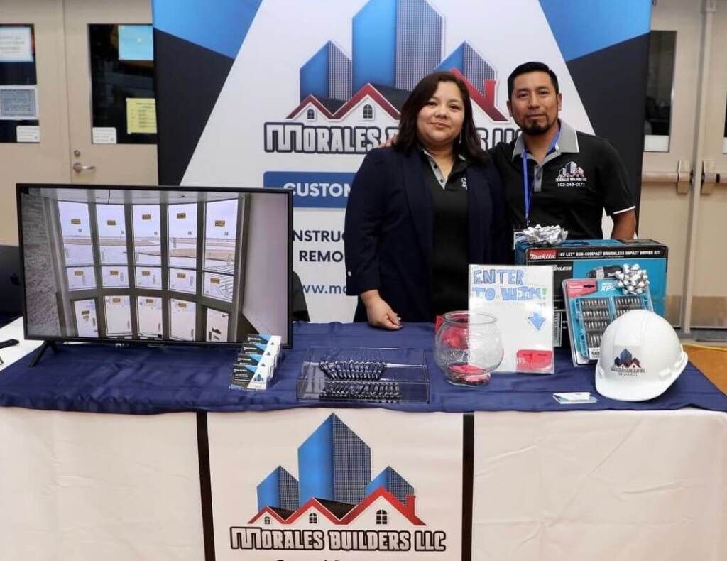 sara-ovalle-marco-morales Sara Ovalle and Marco Morales pose for a photo, smiling, at a table advertising their business.