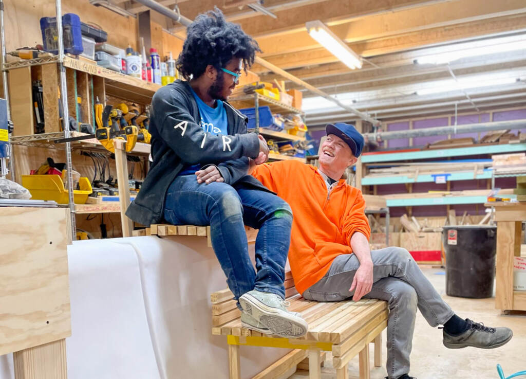 Two people sit on benches in a workshop.