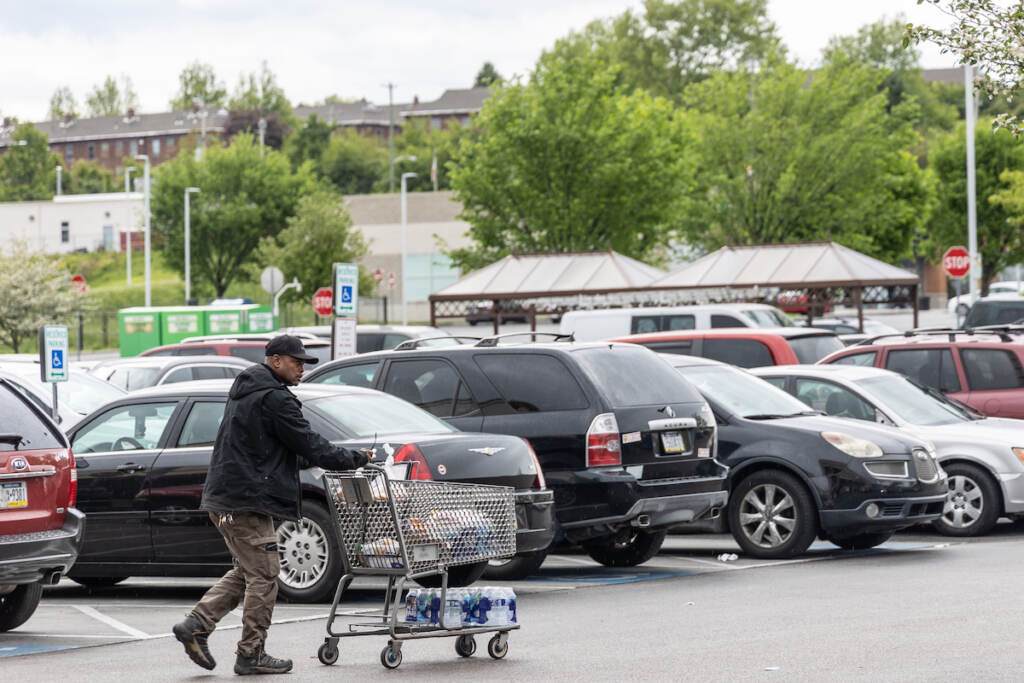 05 03 2023 k paynter bottled water lurk-2 A person pushes a shopping cart in a parking lot. A case of bottled water is visible on the cart.