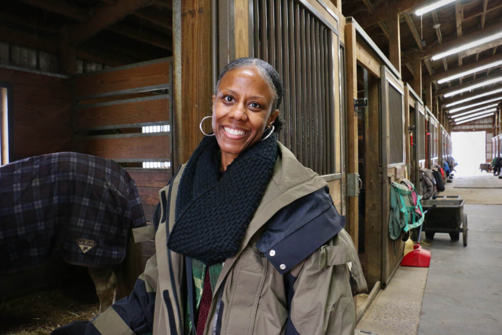 Danielle Allen poses for a photo. Stables are visible behind her.