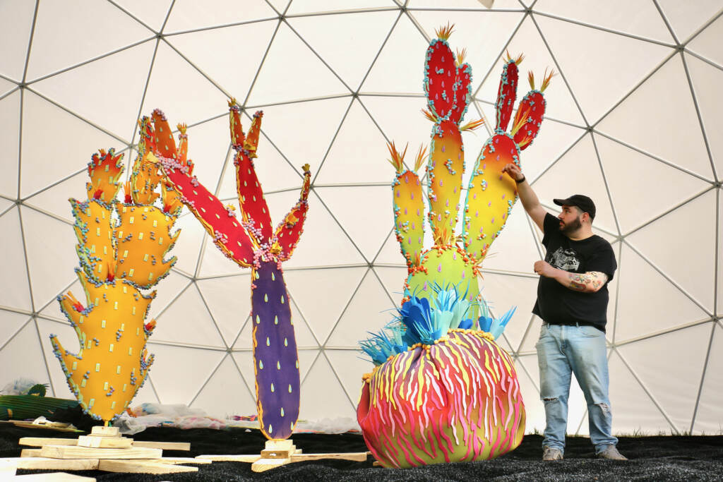 2023 05 01-e lee-maddy geez-philadelphia navy yard-greetings from the mirage set up Matty Geez poses for a photo next to his colorful cacti creations.
