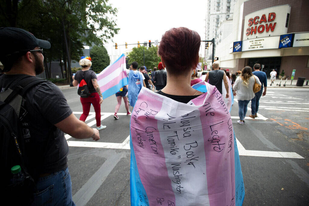 A supporter for the transgender and non-binary community, wearing a transgender flag with handwritten names of black trans women who were killed in 2019 during the Gay Pride Festival's Transgender Rights March in Atlanta on Saturday, Oct. 12, 2019. (AP Photo/Robin Rayne)