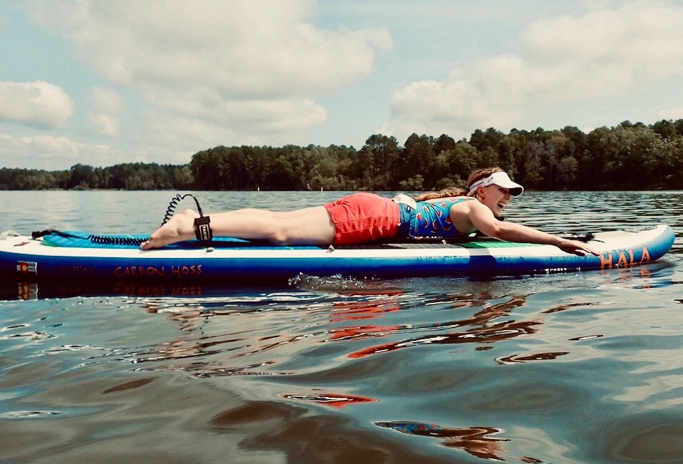 Ashley Yeager lies on a paddle board on a lake. Ashley Yeager lies on a paddle board on a lake.