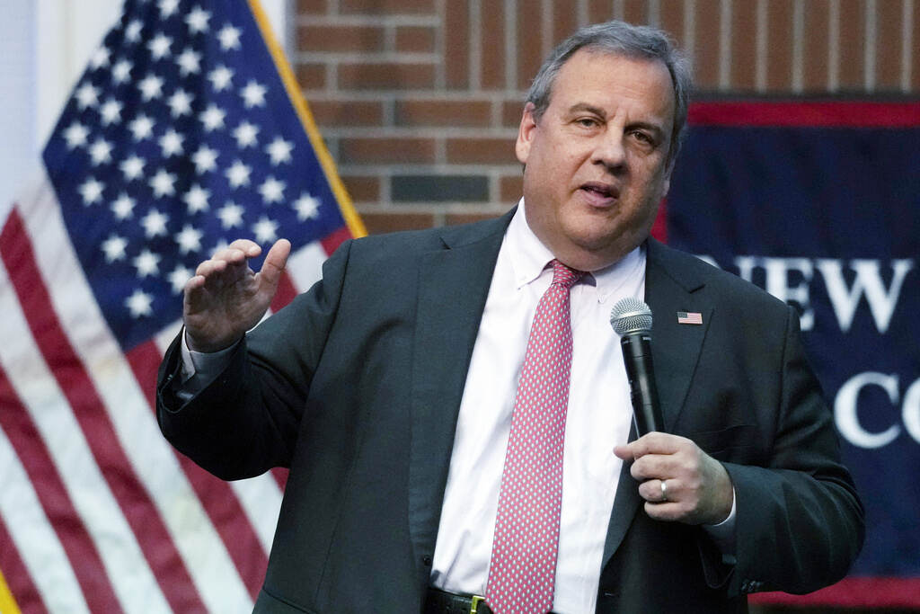 Chris Christie speaks into a microphone. A U.S. flag is visible behind him.