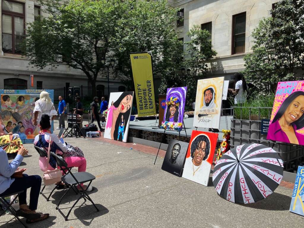 portraits-gv-victims-4 Portraits of people are displayed outdoors, as viewers seated in chairs look on.